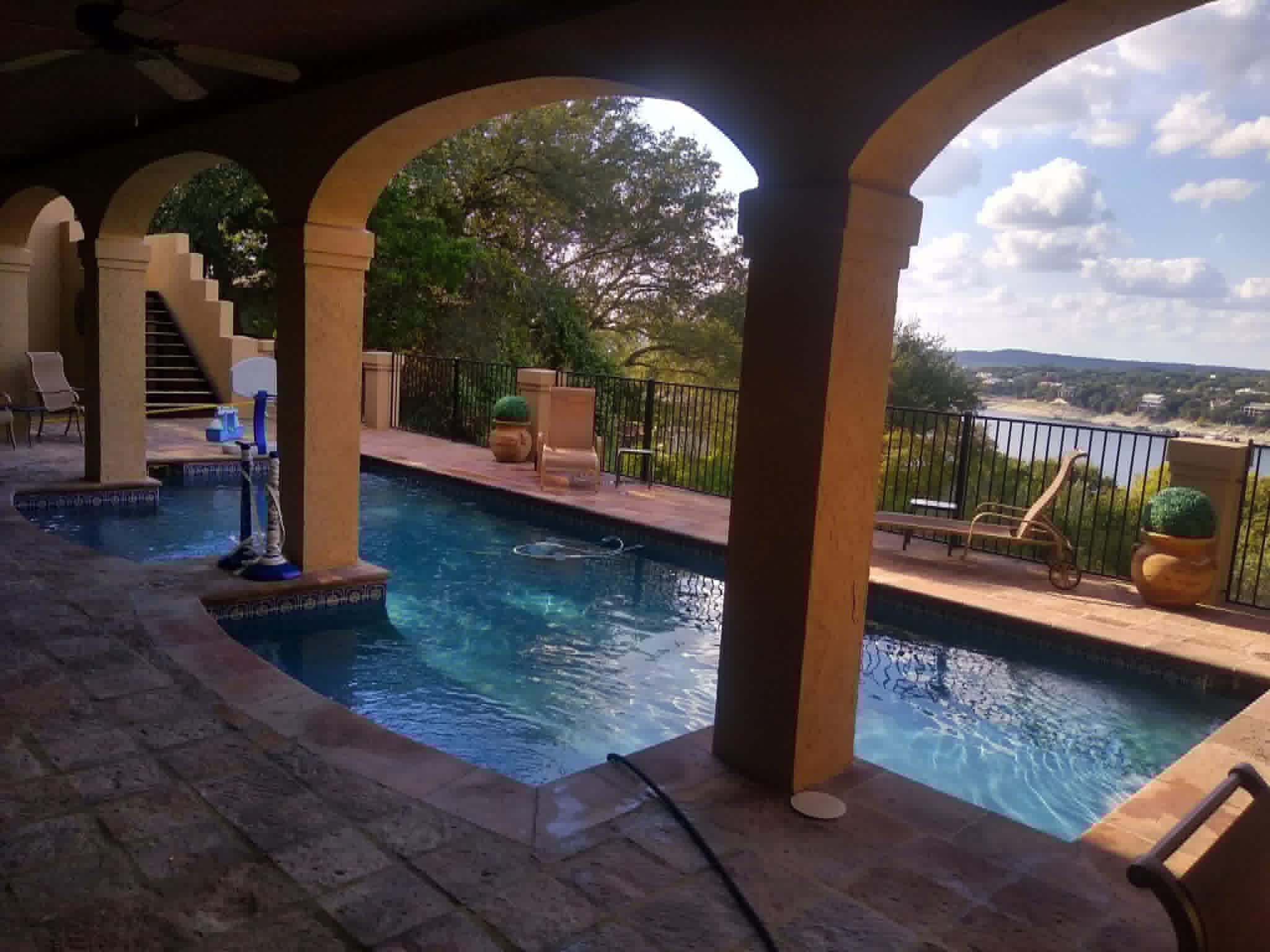 Mediterranean-style pool with arched portico and Lake Travis hill country view — maintained by The Pool Police