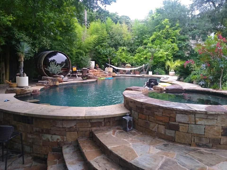 Lush backyard pool with stone-wall surround, barrel sauna, and shaded hammock — weekly service by The Pool Police, West Austin
