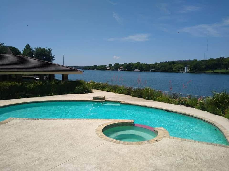 Lakefront residential pool with brown roof house overlooking the water — Hill Country pool service by The Pool Police
